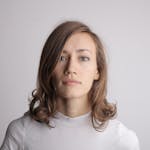 A serene portrait of a woman with brunette hair in a white turtleneck against a white background.