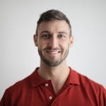 Headshot of a happy man with a beard wearing a red polo shirt against a white background.