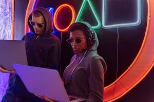 Two cybersecurity experts working on laptops at night with neon lights in the background.