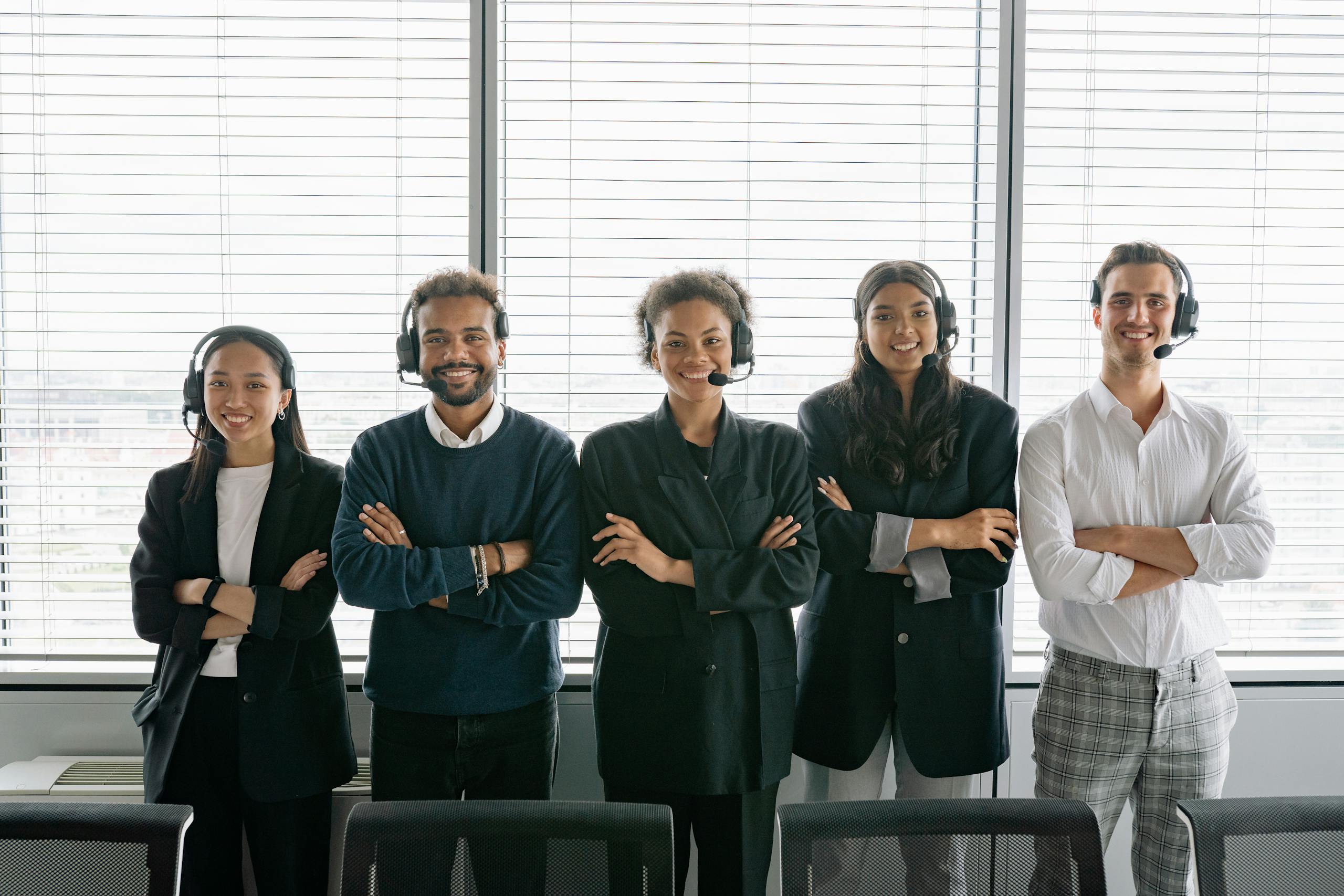 Diverse group of smiling customer service agents wearing headsets in modern office.
